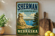 A vintage-style sign for Sherman State Recreation Area in Nebraska, featuring a scenic landscape with a rocky cliff, a lake, and a sailboat.