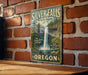 A vintage-style metal sign for Silver Falls State Park in Oregon, featuring a waterfall and forest scenery.