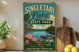 A vintage-style sign for Singletary Lake State Park, featuring a scenic illustration of the lake surrounded by pine trees and mountains, with a red canoe in the water.