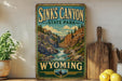 A vintage-style sign for Sinks Canyon State Park in Wyoming, featuring a scenic illustration of a waterfall and mountains.