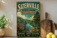 A vintage-style metal sign for Sizerville State Park in Pennsylvania, featuring a scenic landscape with a river and pine trees.