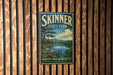 A vintage-style sign for Skinner State Park in Hadley, Massachusetts, featuring a scenic landscape with a lake and mountains.