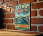 A vintage-style sign for Skyway Fishing Pier State Park in Florida, featuring an illustration of a fish jumping out of the water and a pelican perched on a pier.