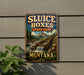 A metal sign with the text "SLUICE BOXES STATE PARK MONTANA" and an illustration of a waterfall and mountains.