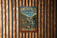 A vintage metal sign for Smith Falls State Park in Nebraska, featuring a scenic image of the waterfall and surrounding landscape.
