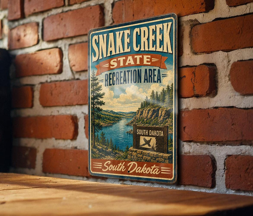 A vintage-style sign for Snake Creek State Recreation Area in South Dakota, featuring a scenic landscape with a river and mountains.