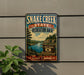 A vintage-style sign for Snake Creek State Recreation Area in South Dakota, featuring a scenic landscape with a river and mountains.