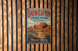 A vintage-style metal sign for Snow Canyon State Park in Utah, featuring a desert landscape with mountains and a pine tree.