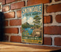 A vintage-style sign for Snowdale State Park in Oklahoma, featuring a scenic landscape with mountains, a lake, and a tree.