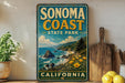 A vintage-style sign for Sonoma Coast State Park in California, featuring a scenic coastal landscape with rocky cliffs, a beach, and a pine tree.