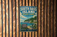 A vintage metal sign for South Bass Island State Park in Ohio, featuring a scenic image of a beach and lake with a lighthouse.