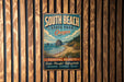 A vintage-style metal sign for South Beach State Park in Oregon, featuring a scenic coastal landscape with mountains, water, and beach.
