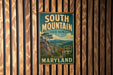 A vintage metal sign for South Mountain State Park in Maryland, featuring a scenic mountain landscape and the text "Beautiful Maryland".
