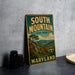 A vintage metal sign for South Mountain State Park in Maryland, featuring a scenic landscape with mountains, trees, and a waterfall.