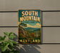 A vintage metal sign for South Mountain State Park in Maryland, featuring a scenic mountain landscape with a pine tree and clouds in the background.