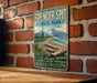 A vintage-style metal sign for Spencer Spit State Park, featuring a scenic landscape with a beach, mountains, and a body of water.