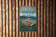 A vintage-style metal sign for Spencer Spit State Park, featuring a scenic landscape with a beach, mountains, and a body of water.