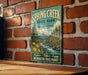 A vintage-style metal sign for Spring Creek State Park in Washington, featuring a scenic landscape with mountains, trees, and a river.