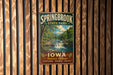 A vintage metal sign for Springbrook State Park in Iowa, featuring a scenic landscape with a waterfall and forest.