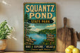 A vintage-style sign for Squantz Pond State Park in Connecticut, featuring a scenic landscape with a lake, trees, and mountains.