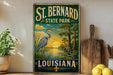 A vintage-style sign for St. Bernard State Park in Louisiana, featuring a blue heron and a sunset landscape.