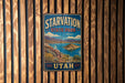 A vintage metal sign for Starvation State Park in Utah, featuring a scenic landscape with mountains, a lake, and a small island.
