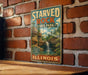 A vintage-style metal sign for Starved Rock State Park in Illinois, featuring a scenic image of a waterfall and forest.