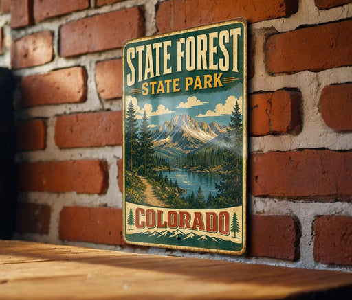 A vintage-style metal sign for State Forest State Park in Colorado, featuring a scenic mountain landscape with pine trees and a lake.