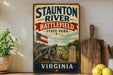a vintage-style metal sign for Staunton River Battlefield State Park in Virginia, with a cannon and a wooden paddle on a shelf.