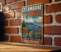 A vintage-style sign for Steamboat Lake State Park, featuring a scenic illustration of the lake surrounded by mountains and wildlife.
