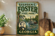 A vintage-style sign for Stephen C. Foster State Park in Georgia, featuring a portrait of a man and an illustration of a river with a steamboat.