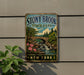 A vintage-style metal sign for Stony Brook State Park in New York, featuring a scenic landscape with a bridge, waterfalls, and trees.