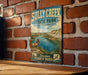 A vintage-style metal sign for Sully Creek State Park in North Dakota, featuring a scenic illustration of a mountain landscape with a river and a ram.