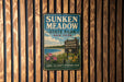 A vintage metal sign for Sunken Meadow State Park in New York, featuring a scenic landscape with a beach, flowers, and a blue sky.