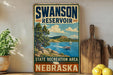 A vintage-style sign for the Swanson Reservoir State Recreation Area in Nebraska, featuring a scenic landscape with a lake, mountains, and a sailboat.