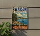 A vintage-style sign for the Swanson Reservoir State Recreation Area in Nebraska, featuring a scenic landscape with a lake, mountains, and a sailboat.