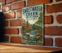 A vintage-style metal sign for Sweetwater Creek State Park in Georgia, featuring a scenic illustration of a waterfall and lush greenery.