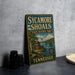 A vintage-style metal sign for Sycamore Shoals State Historic Park in Tennessee, featuring an illustration of a historic fort and a river.