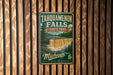 A vintage metal sign for Tahquamenon Falls State Park in Michigan, featuring a waterfall and forest landscape.