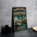 A vintage-style metal sign for Tarpon Springs Heritage State Park in Florida, featuring a boat and palm trees, is displayed on a gray countertop next to a stack of black camera lenses.