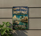 A vintage-style metal sign for Tarpon Springs Heritage State Park in Florida, featuring a boat and palm trees, mounted on a wall.