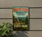 A vintage-style metal sign for Taun sauk Mountain, the highest point in Missouri, with a scenic mountain landscape and pine trees.