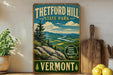 A vintage-style metal sign for Theftord Hill State Park in Vermont, featuring a scenic mountain landscape with pine trees and a winding river.