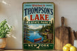A vintage-style metal sign welcoming visitors to Thompson's Lake State Park in New York, featuring a scenic image of the lake and surrounding forest.