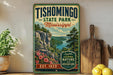 A vintage-style metal sign for Tishomingo State Park in Mississippi, featuring a scenic landscape with a river and mountains.