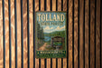 A vintage metal sign for Tolland State Forest in Massachusetts, featuring a scenic landscape with pine trees, a lake, and mountains.