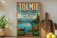 A vintage-style sign for Tolmie State Park in Washington, featuring a scenic mountain landscape with a lake and wooden dock.