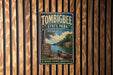 A vintage metal sign for Tombigbee State Park in Mississippi, featuring a scenic image of a river and a canoe, mounted on a wooden wall.