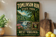 A vintage-style sign for Tomlinson Run State Park in West Virginia, featuring a scenic landscape with a waterfall and pine trees.