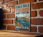 A vintage metal sign for Tongue River Reservoir State Park in Montana, featuring a scenic landscape with mountains, a river, and a boat.